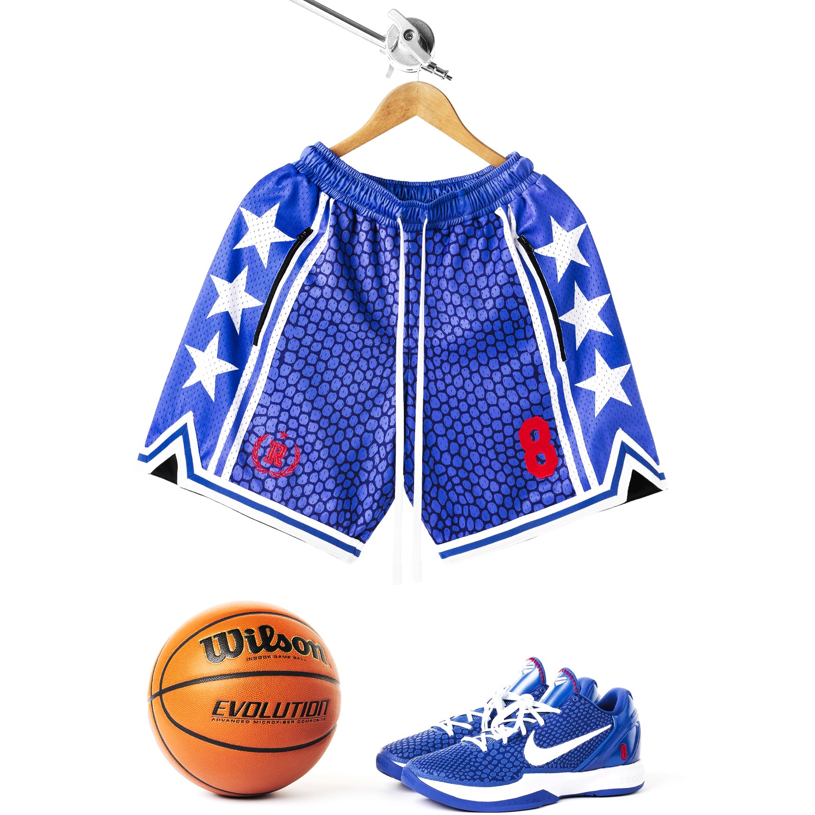 Heavyweight mesh basketball shorts with mamba snakeskin pattern, white stars, red embroidered number 8, rib knit trim, and long drawstrings—hanging on hanger with white background and a basketball, and Nike Kobe 6 Protro Game Royal sneakers