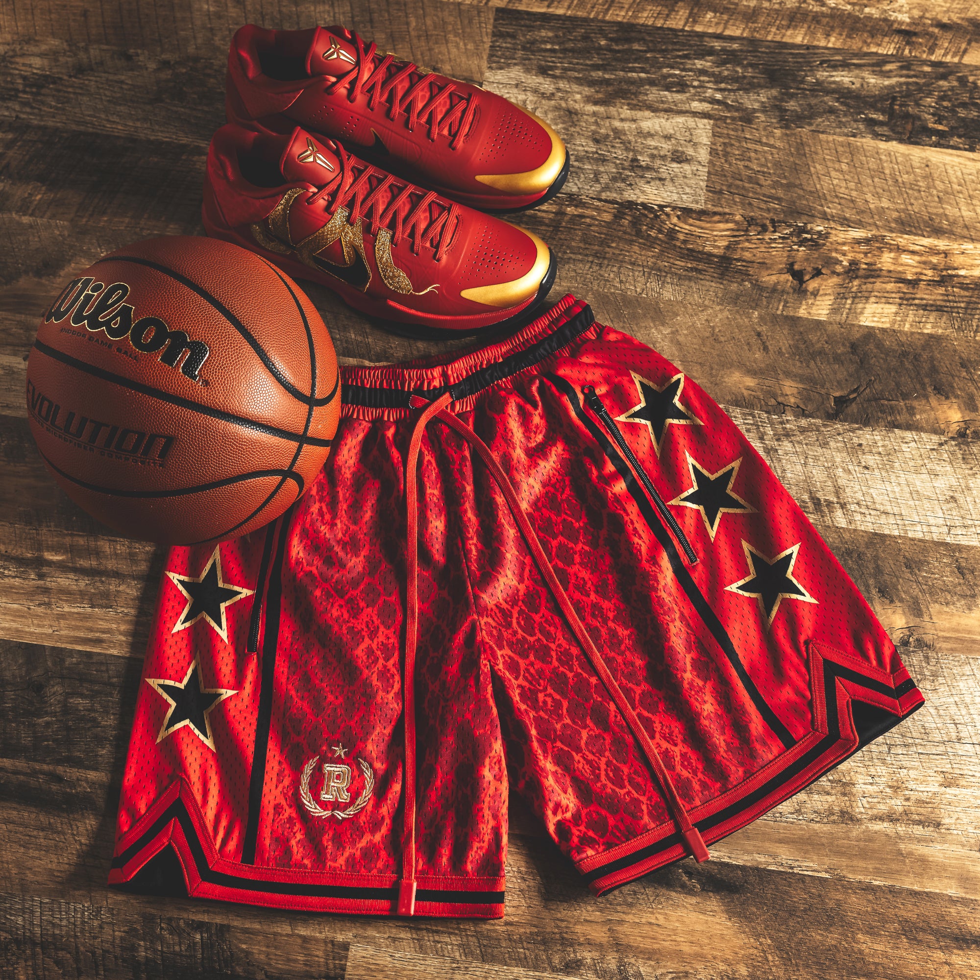 Year of the Snake Red NBA Swingman Heavyweight Mesh Basketball Shorts with zippered pockets and long red drawstrings, red snakeskin pattern, lay flat on hardwood floor with Wilson Evolution basketball and red Nike Kobe 5 Year of the Mamba shoes