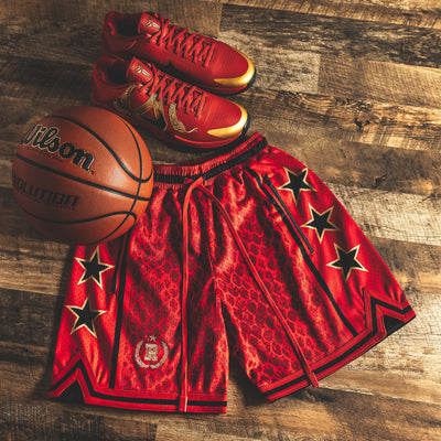 Year of the Snake Red NBA Swingman Heavyweight Mesh Basketball Shorts with zippered pockets and long red drawstrings, red snakeskin pattern, lay flat on hardwood floor with Wilson Evolution basketball and red Nike Kobe 5 Year of the Mamba shoes