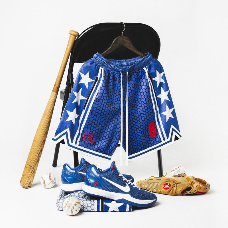 Heavyweight mesh basketball shorts with mamba snakeskin pattern, white stars, red embroidered number 8, rib knit trim, and long drawstrings—hanging on hanger with white background and a basketball, and Nike Kobe 6 Protro Game Royal sneakers